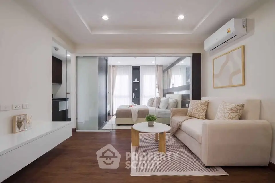 Modern living room with elegant decor and glass partition leading to bedroom, featuring cozy seating and stylish accents.