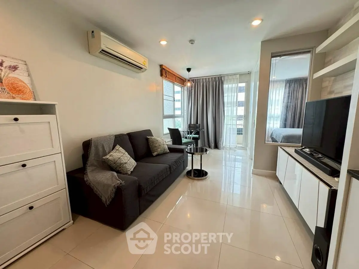 Modern living room with sleek design, featuring a cozy sofa, air conditioning, and a view into the bedroom.