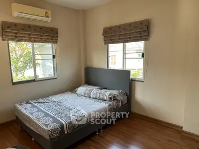 Cozy bedroom with wooden flooring and ample natural light from two windows.