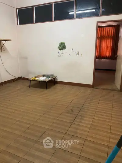 Spacious room with wooden flooring and wall art, leading to a sunlit area with curtains.