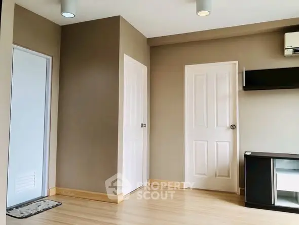 Spacious modern room with wooden flooring and neutral walls, featuring sleek shelving and air conditioning.