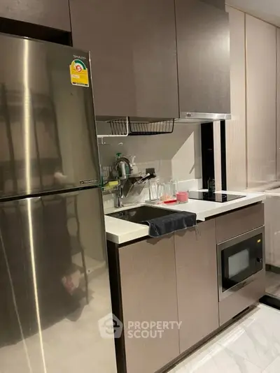 Modern kitchen with sleek cabinets, stainless steel fridge, and built-in microwave in a compact layout.