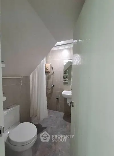 Compact bathroom with shower under staircase, featuring modern fixtures and neutral tiles.