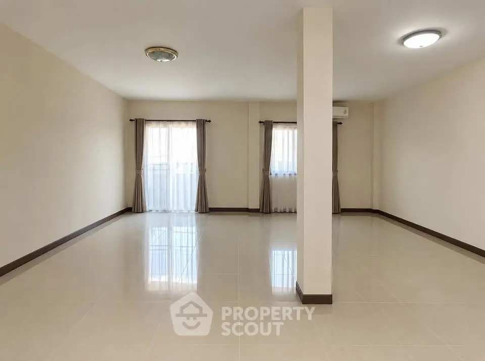 Spacious empty living room with large windows and polished tile flooring.