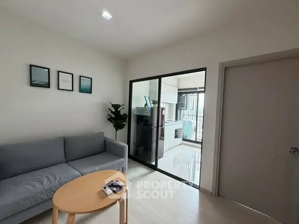 Modern living room with gray sofa and open kitchen layout, featuring sleek design and natural light.
