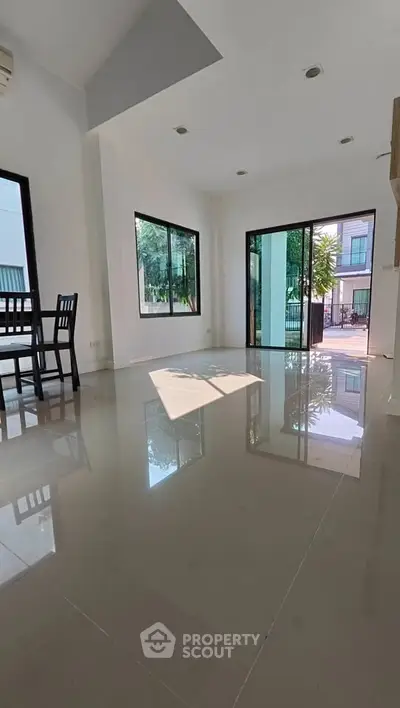 Spacious modern living room with large windows and glossy tiled floors, offering abundant natural light.