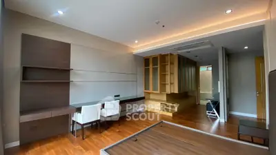 Modern living room with wooden flooring and built-in shelves, featuring a sleek design and ample natural light.