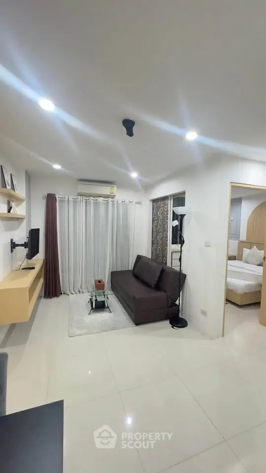 Modern living room with sleek furniture and open layout, leading to a cozy bedroom.