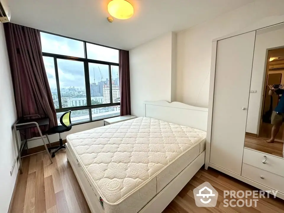 Spacious bedroom with large window offering stunning city views and modern furnishings.