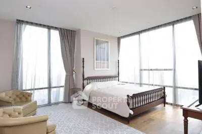 Spacious bedroom with large windows and elegant furnishings in modern apartment.