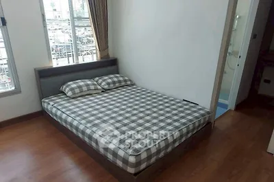 Cozy bedroom with checkered bedding and wooden flooring, featuring ample natural light from large windows.