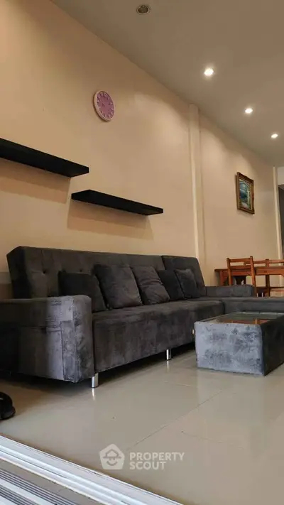 Modern living room with sleek gray sofa, wall shelves, and dining area in open layout.