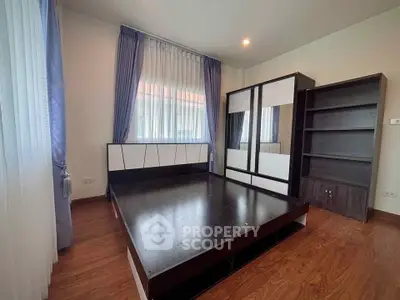 Spacious bedroom with modern bed frame and ample natural light, featuring elegant curtains and wooden flooring.