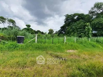 Lush green land plot with fencing under a cloudy sky, ideal for development.