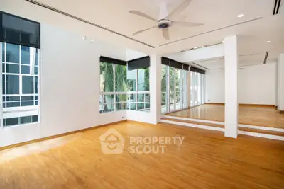 Spacious modern living room with wooden flooring and large windows offering natural light.