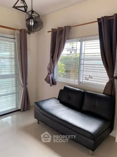 Modern living room with sleek black sofa and large windows for natural light.