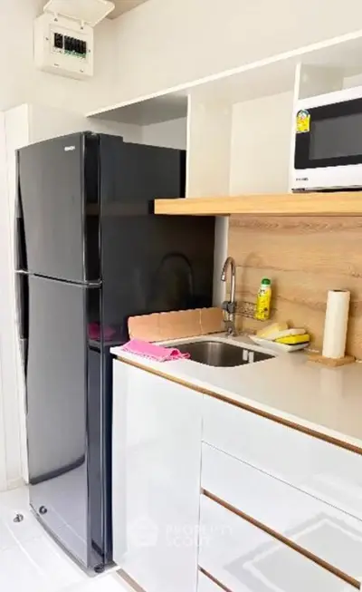 Modern kitchen with sleek black fridge and microwave, featuring white cabinetry and wooden accents.