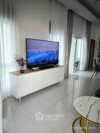 Modern living room with sleek TV setup and elegant decor, featuring large windows and stylish furniture.