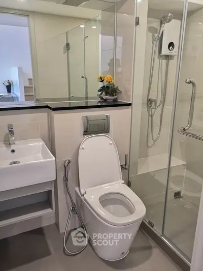 Modern bathroom with glass shower, sleek sink, and toilet in a contemporary apartment.
