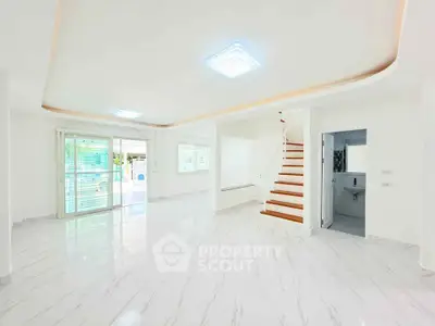 Spacious modern living room with elegant staircase and large windows, perfect for natural light.