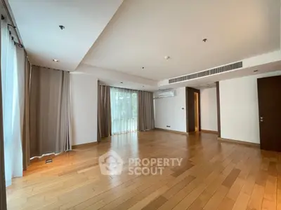Spacious empty living room with wooden floors and large windows in modern apartment.