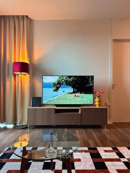 Stylish living room with modern decor, featuring a flat-screen TV, elegant lamp, and chic glass coffee table.
