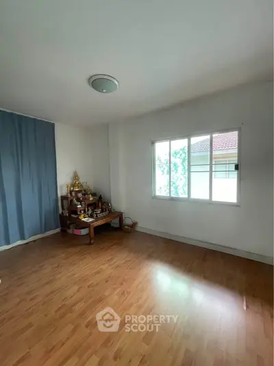 Spacious room with wooden flooring and large window, ideal for versatile use.