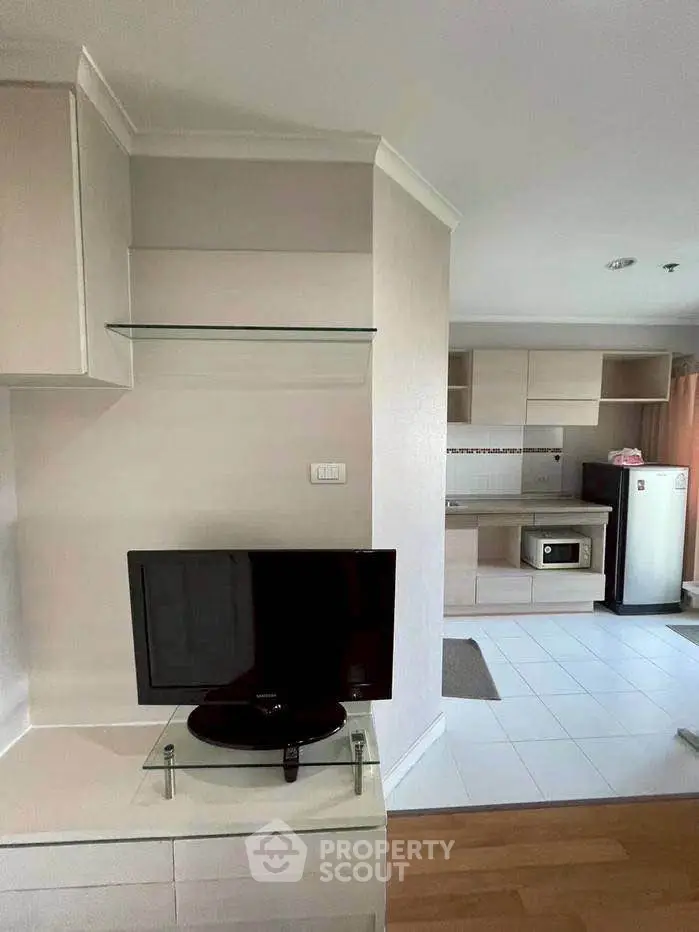 Modern apartment interior with TV and kitchen area, featuring sleek cabinetry and appliances.