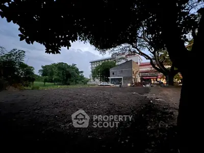 Spacious land plot with potential for development surrounded by lush greenery and nearby buildings.