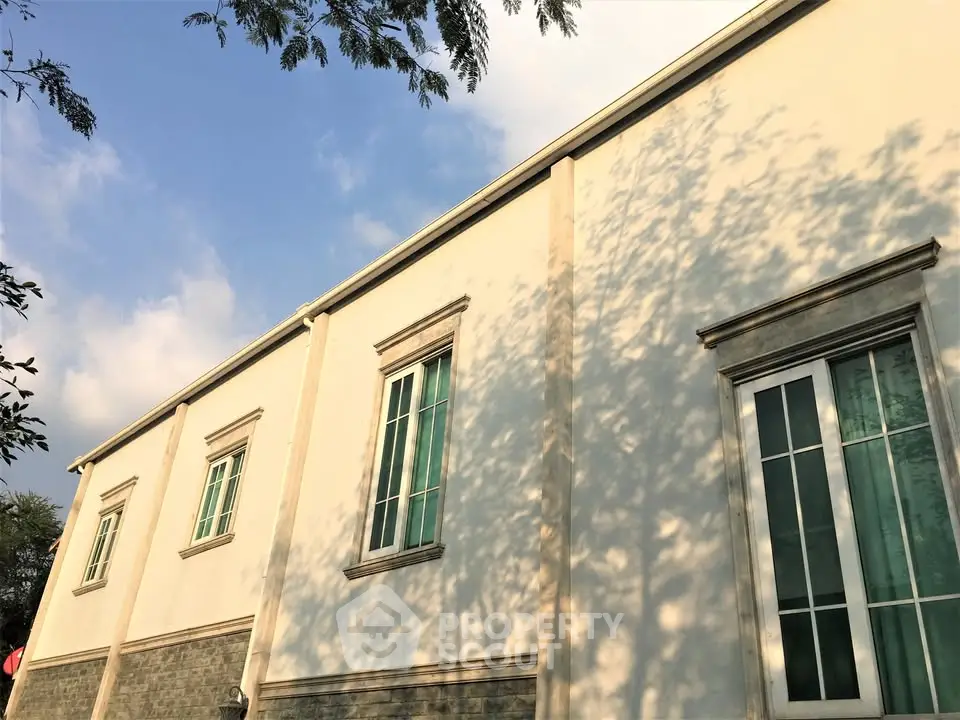 Elegant building exterior with classic windows and lush greenery, showcasing architectural charm under a clear blue sky.