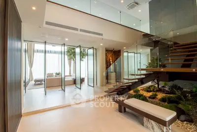 Luxurious modern living room with glass walls and indoor garden, featuring elegant staircase and natural light.
