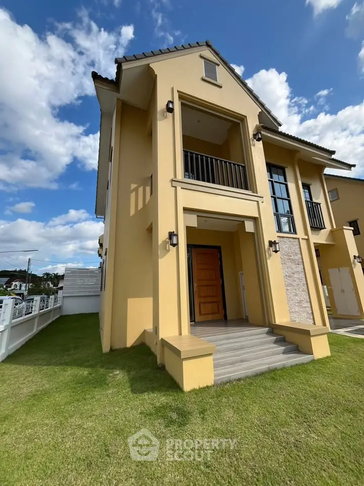 Stunning modern two-story house with spacious balcony and lush green lawn under a clear blue sky.