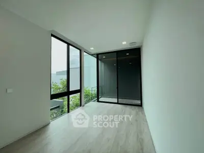 Spacious modern room with large windows and balcony access, featuring sleek flooring and minimalist design.