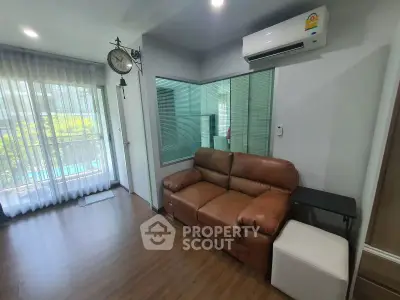 Modern living room with leather sofa and air conditioning, featuring large windows and stylish decor.