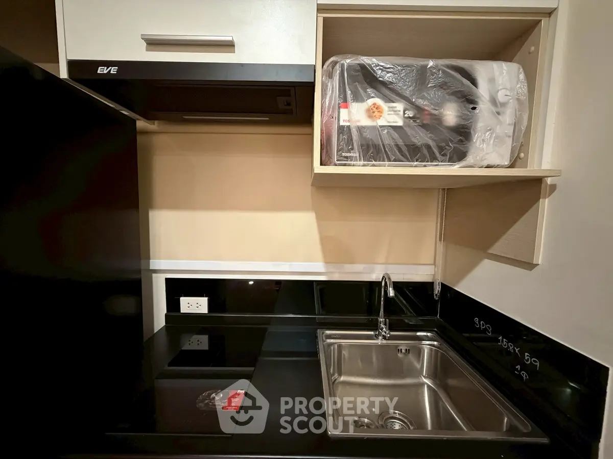Modern kitchen with sleek black countertops and stainless steel sink, featuring a compact design and built-in appliances.