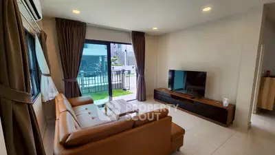 Modern living room with leather sofa and large TV, featuring garden view through sliding glass doors.
