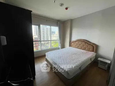 Spacious bedroom with large window offering city view, featuring a comfortable bed and wooden flooring.