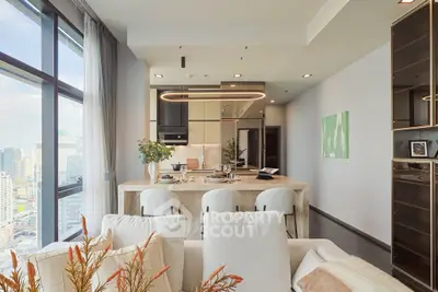 Luxurious modern living room with open kitchen and city view, featuring elegant decor and natural light.