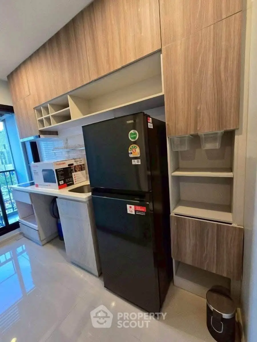Modern kitchen with sleek black fridge and wooden cabinets, featuring a microwave and ample storage space.