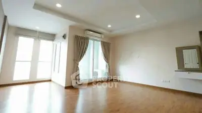 Spacious empty living room with wooden flooring and large windows for natural light.