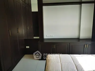 Spacious bedroom with elegant dark wood built-in wardrobes and cozy bed.