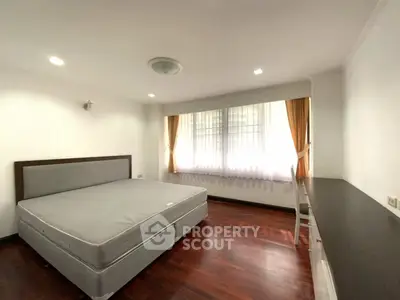Spacious bedroom with large window and wooden flooring in modern apartment.