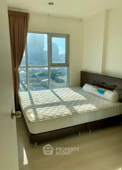 Bright bedroom with large window and city view, featuring a comfortable bed and elegant curtains.