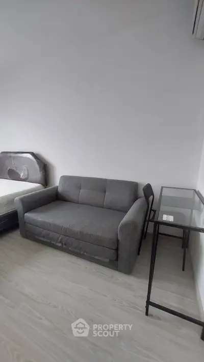 Cozy bedroom with compact sofa and glass desk, perfect for urban living.