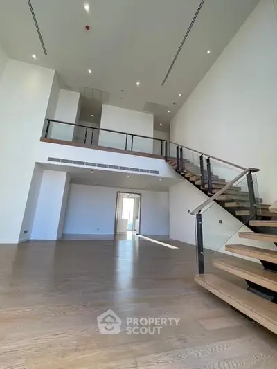 Spacious modern living room with high ceilings and elegant staircase in luxury apartment.