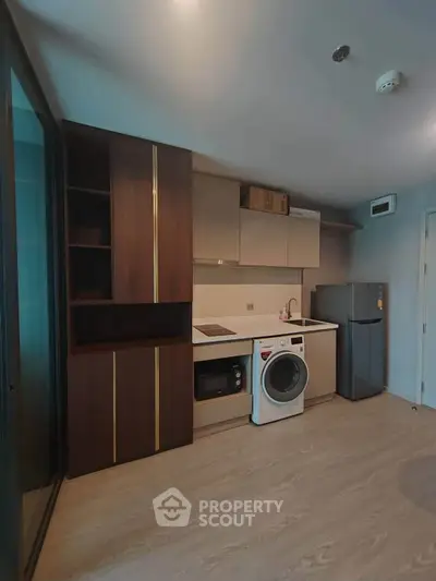 Modern kitchen with sleek cabinetry, washing machine, and compact fridge in a stylish apartment.