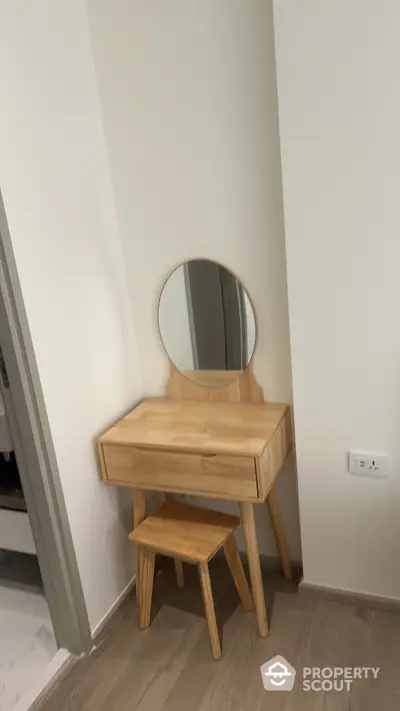 Charming corner with a modern wooden vanity table and matching stool, set against a clean, white wall and warm wooden flooring, perfect for personal grooming.