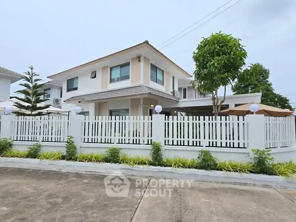 Modern two-story house with white fence and lush greenery in a suburban setting.