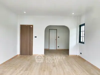 Spacious empty room with wooden flooring and arched doorway, perfect for customization.