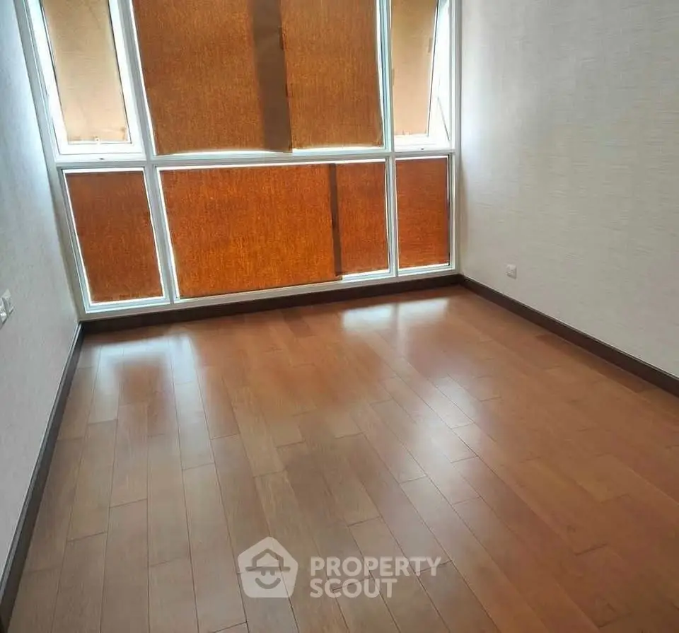 Spacious empty room with wooden flooring and large windows.